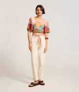 Pantalón mom color crudo confeccionado en sarga de algodón BCI, con bolsillos delanteros y traseros, cierre con botón y cremallera, y pañuelo estampado a modo de cinturón.