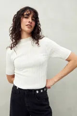 Top de manga corta color blanco, tejido con textura acanalada, cuello alto y terminaciones onduladas en mangas y ruedo.