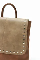Mochila de cuero sintético color marrón y beige, con solapa con cierre de botón a presión y tachas plateadas.