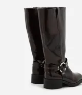 Bota biker de caña alta color marrón oscuro, con puntera redonda, taco bajo y detalle de hebilla con aro metálico en el lateral.