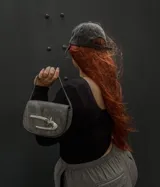 Mini bag gris con correa fina y cierre con forma de gancho plateado.