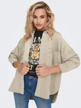 Camisa oversize color beige de pana con cuello clásico, cierre frontal con botones, mangas largas con puños abotonados, dos bolsillos con botón en el pecho y ruedo asimétrico.