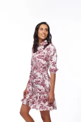 Vestido corto camisero blanco con estampado de motivos campestres en color bordó. Tiene cuello camisero, mangas 3/4, lazo en la cintura y volado en el ruedo.