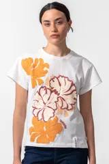 Remera blanca de algodón con cuello redondo y mangas cortas. Estampado frontal con flores en tonos naranja y bordó, y logo de la marca en el ruedo.