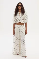 Pantalón de lino color crudo con lunares marrones, de corte ancho y tiro medio-alto, con elástico en la parte trasera de la cintura.