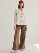 Camisa blanca de algodón con cuello mao, mangas largas abullonadas y cierre frontal con botones de madera. Presenta detalles de bordado calado en el canesú.