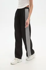 Pantalón de algodón negro, holgado, de calce medio, con cintura elástica y cordón ajustable. Presenta tres rayas blancas verticales en los laterales.