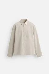 Camisa regular fit confeccionada en tejido con mezcla de algodón. Color beige con finas rayas verticales blancas. Cuello italiano, manga larga con puños abotonados, bolsillo de parche en el pecho y cierre frontal con botones.