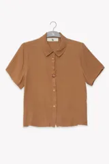 Camisa color marrón claro con cuello clásico, cierre frontal con botones y mangas cortas.