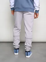 Pantalón de jogging gris claro, corte clásico, con logo de la marca Umbro bordado en negro en el muslo izquierdo y costuras en contraste.