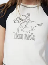 Remera color crema con mangas cortas negras tipo ranglán y estampado de jinete con la palabra 'Bandida'.