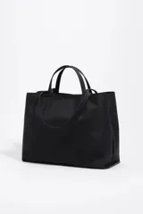 Bolso shopper grande de nylon negro, con estructura blanda, doble asa de mano y correa larga ajustable para llevar al hombro. Presenta un logo metálico con el texto "BIMBA Y LOLA" en la parte frontal inferior.