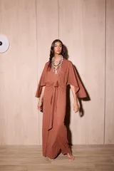 Vestido largo tipo kimono de color marrón, confeccionado en tela de punto texturada. Posee mangas amplias y abiertas, escote en V pronunciado y un lazo ajustable en la cintura para definir la silueta.