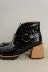 Botas cortas de cuero negro con textura tipo cocodrilo, caña alta, cierre con hebilla y taco de madera.