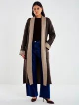 Saco largo de tejido de punto marrón oscuro con micro lentejuelas sutiles. Presenta un cuello chal ancho en color beige/tostado, puños doblados a tono y bolsillos aplicados. Se ajusta con un lazo o faja del mismo tejido principal.