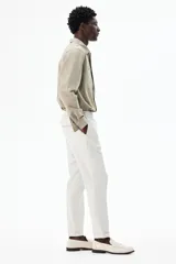 Pantalón de vestir gris claro, de corte slim fit, con cintura elástica y cordón ajustable. Presenta bolsillos laterales y traseros ribeteados, pliegues cosidos y doblez en el bajo.