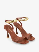 Sandalias de tacón negras con tira delgada sobre los dedos y pulsera tobillera con adorno tubular plateado.