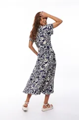 Vestido midi con estampado floral en tonos azul marino y blanco, escote en V, mangas cortas y falda acampanada con cinturón ajustable.
