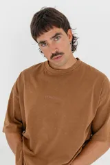 Remera color marrón con efecto gastado, corte holgado, mangas cortas y estampado en la espalda con dos rostros enfrentados y la palabra "Forgive".
