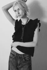 Remera negra sin mangas con volados en los hombros y escote en V. Incluye un collar largo de cuentas con un nudo decorativo. Jeans de tiro bajo.