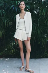 Chaqueta blanca de punto con cuello redondo y manga larga. Tiene vivos negros en el cuello, el borde frontal y los puños. Se cierra con botones en el frente.