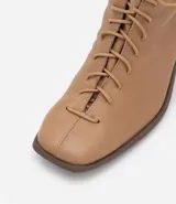 Bota de cuero color marrón claro, de caña media, con puntera cuadrada, taco bloque y cierre con cordones y cremallera.