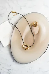 Collar de acero quirúrgico dorado con colgante moderno y cordón negro, ideal para un look versátil.