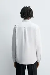 Camisa de algodón color celeste claro, corte regular fit, con cuello abotonado (button-down), manga larga con puño abotonado y bolsillo de parche en el pecho izquierdo.