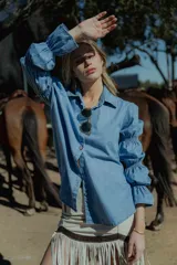 Camisa celeste de jean fino, con cuello clásico, cierre frontal con botones y mangas largas abullonadas con puños elastizados.