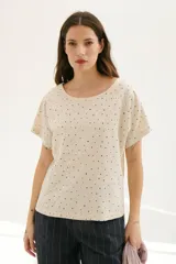 Blusa color crema con estampado de lunares negros, cuello redondo y mangas cortas.