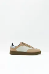 Zapatillas deportivas bajas color beige con paneles laterales en blanco y contrafuerte plateado.