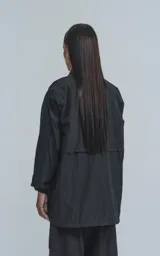 Campera negra de corte recto, con cuello camisero, cierre frontal con botones a presión, mangas largas con puños elásticos, un bolsillo superior con solapa y dos bolsillos inferiores con ribete blanco.