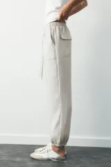 Pantalón jogger color gris claro, de tiro alto con cintura elástica ajustable con cordones, bolsillos delanteros y traseros con solapa, y puños elásticos en el bajo.