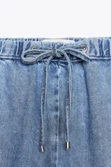 Pantalón de jean azul oscuro, de tiro medio, corte ancho y largo, estilo jogger con cintura elástica ajustable con cordones, bolsillos delanteros de vivo y bolsillos de parche en la espalda.