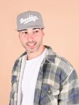 Gorro gris con visera plana y bordado frontal con la palabra "Brooklyn" en blanco.