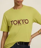 Remera verde claro de algodón con cuello redondo y mangas cortas. Estampado frontal con la palabra "TOKYO" en color borgoña y la frase "Where Zen Meets The Neón" debajo.
