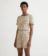 Blusa de crepé color beige con estampado de lunares de colores, cuello redondo con ribete negro, manga corta abullonada, bolsillo de parche en el pecho y bajo mullet con aberturas laterales.