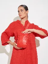 Bandolera roja de cuero sintético, con correa ajustable y cierre superior.