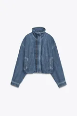 Chaqueta corta de denim azul con cuello alto, manga larga con hombros caídos, bolsillos laterales, bajo con elástico y cierre frontal con cremallera y botones ocultos.
