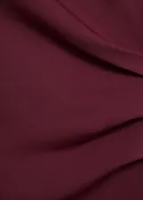 Vestido midi entallado color bordó, con cuello alto, sin mangas y fruncido lateral. Confeccionado en poliéster y elastano.