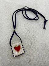 Collar con dije rectangular bordado con un corazón rojo y detalles de mostacillas de colores.