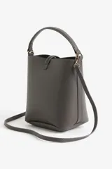 Cartera gris tipo bucket con asa corta y correa larga extraíble. Tiene cierre con trabilla y herraje metálico dorado. Interior forrado.