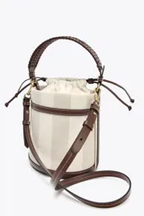Bolso tipo bucket cilíndrico a rayas verticales en tonos beige y blanco, con asa de mano trenzada color marrón y asa de hombro extraíble. Incluye bolso de tela interior y pespuntes a contraste.