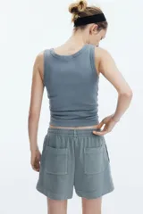 Short gris de felpa de algodón con efecto lavado, corte holgado, cintura elástica con cordón ajustable, bolsillos laterales y traseros, y aberturas laterales en el ruedo.