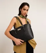 Bolso shopper grande de poliuretano negro con textura acolchada. Tiene correa de mano con detalles de hebilla y remaches plateados. Cierre superior con cremallera y forro de poliéster.