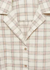 Blusa corta de manga corta con diseño a cuadros en tonos beige y blanco. Presenta cuello camisero, cierre frontal con botones y lazo en la parte inferior.