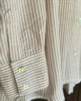 Camisa a rayas verticales, con cuello clásico y cierre frontal con botones.