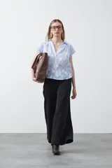 Blusa de algodón con rayas verticales celestes y blancas, con apliques florales en relieve blancos. Presenta cuello camisero y escote en V, con mangas cortas y calce holgado.