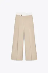Pantalón color beige de tiro alto con cintura combinada en blanco, pinzas delanteras y pernera ancha. Cierre frontal con cremallera y botón.