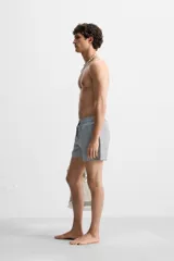 Short de baño con textura seersucker a rayas verticales azul marino y blanco. Tiene cintura elástica ajustable con cordón, bolsillos frontales y traseros, aberturas laterales en el bajo y forro interior.